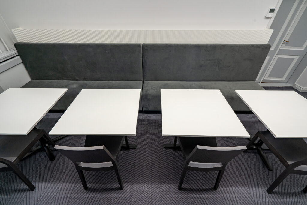 Valgete laudade ja tumedate toolidega istumisala halli seinapadjaga