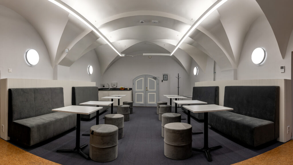 Hele kaarvõlvidega puhkeruum laudade ja hallide istmete ning tumbadega.