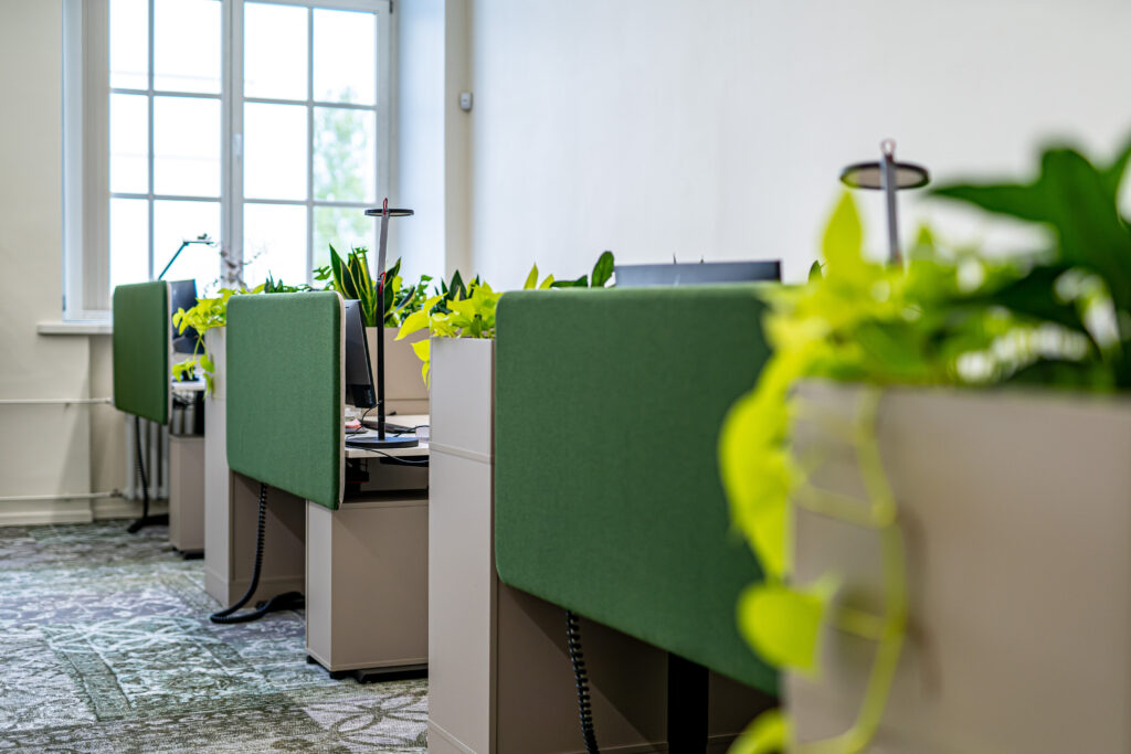 Roheliste vaheseinte ja rohkete taimedega avatud kontoritööalad heledas ruumis