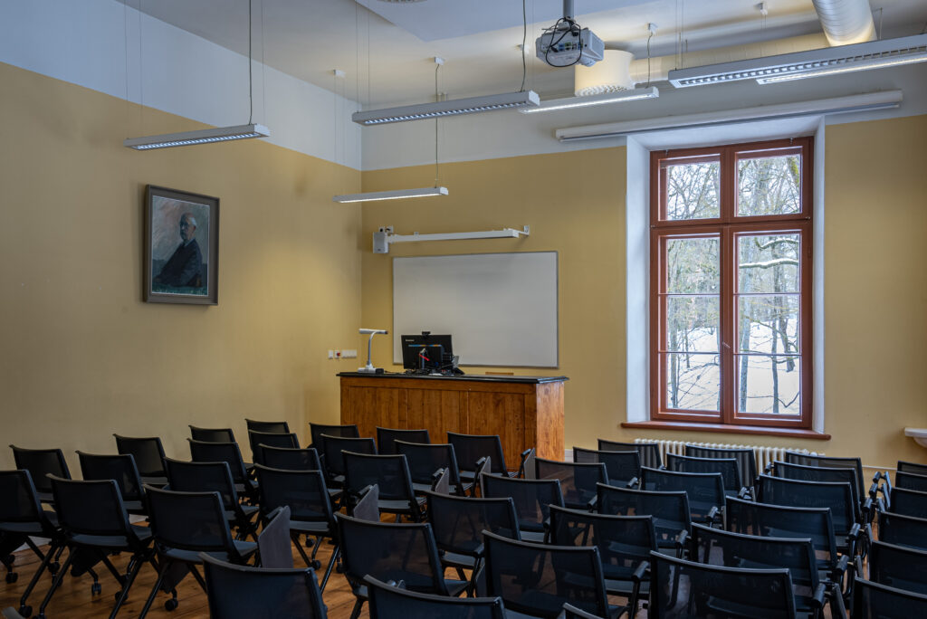 Klassiruum: kollased seinad, mustad toolid, puitne kõnepult