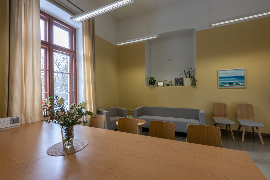 Hubane nõupidamisruum: pikk laud, hallid sohvad, soe valgus