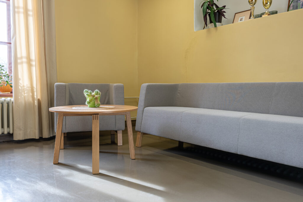 Valge ja halli tonaalsusega puhkeala lihtsa lauaga ning päikeselise aknaga